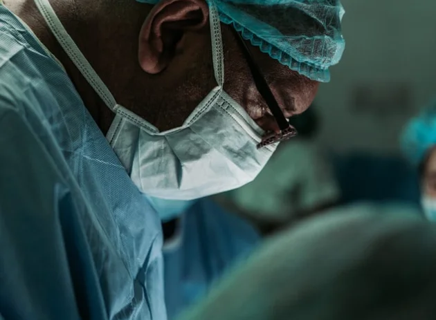 Surgeon wearing surgical mask, cap, and scrubs focused during an operation in the operating room